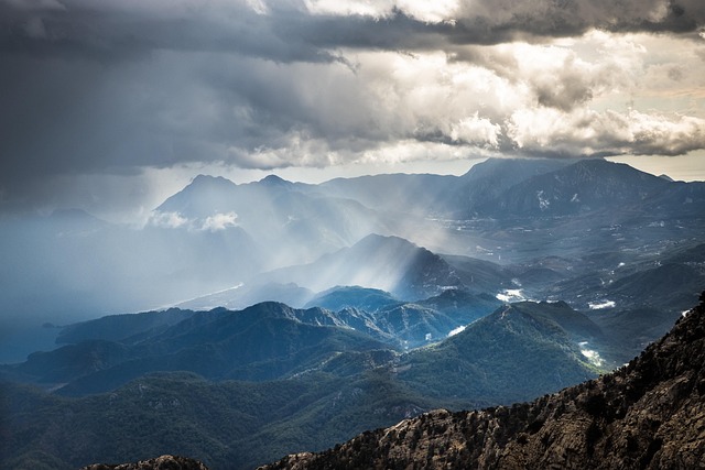 Sunlight breaking through clouds over jagged mountain peaks, revealing a grand panorama.